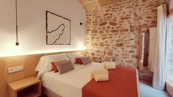 A bedroom with a stone wall, a bed with white bedding, a wooden nightstand, and a map artwork.