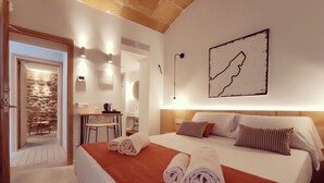 Ein Hotelzimmer mit einem großen Bett, einem Schreibtisch mit Stuhl, einem kleinen Tisch und einer Steinwand.
