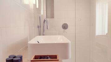 Un baño moderno con un lavamanos grande de color blanco, un cabezal de ducha de mano y un mueble de tocador de madera con cajones.