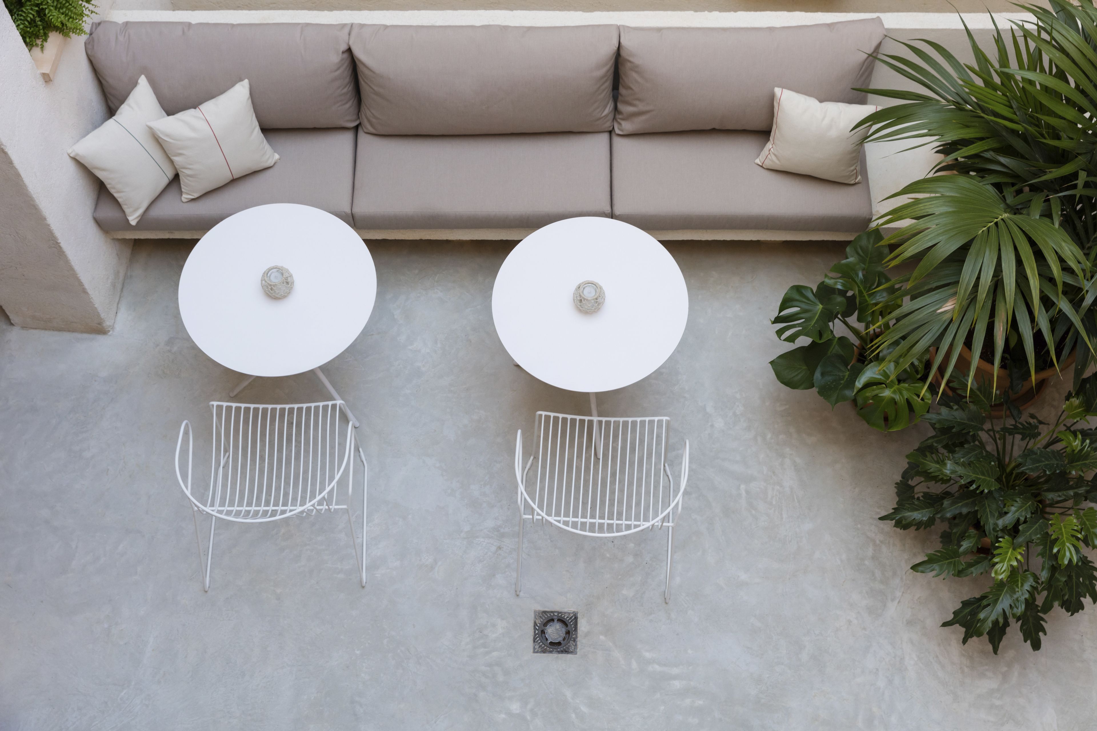 A beige sofa with two white round tables and metal chairs, a potted plant, and a concrete floor.