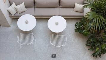 A beige sofa with two white round tables and metal chairs, a potted plant, and a concrete floor.
