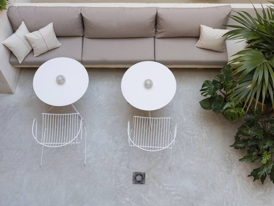 A beige sofa with two white round tables and metal chairs, a potted plant, and a concrete floor.