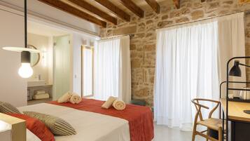 A hotel room with a bed, a desk, a chair, and a stone wall.
