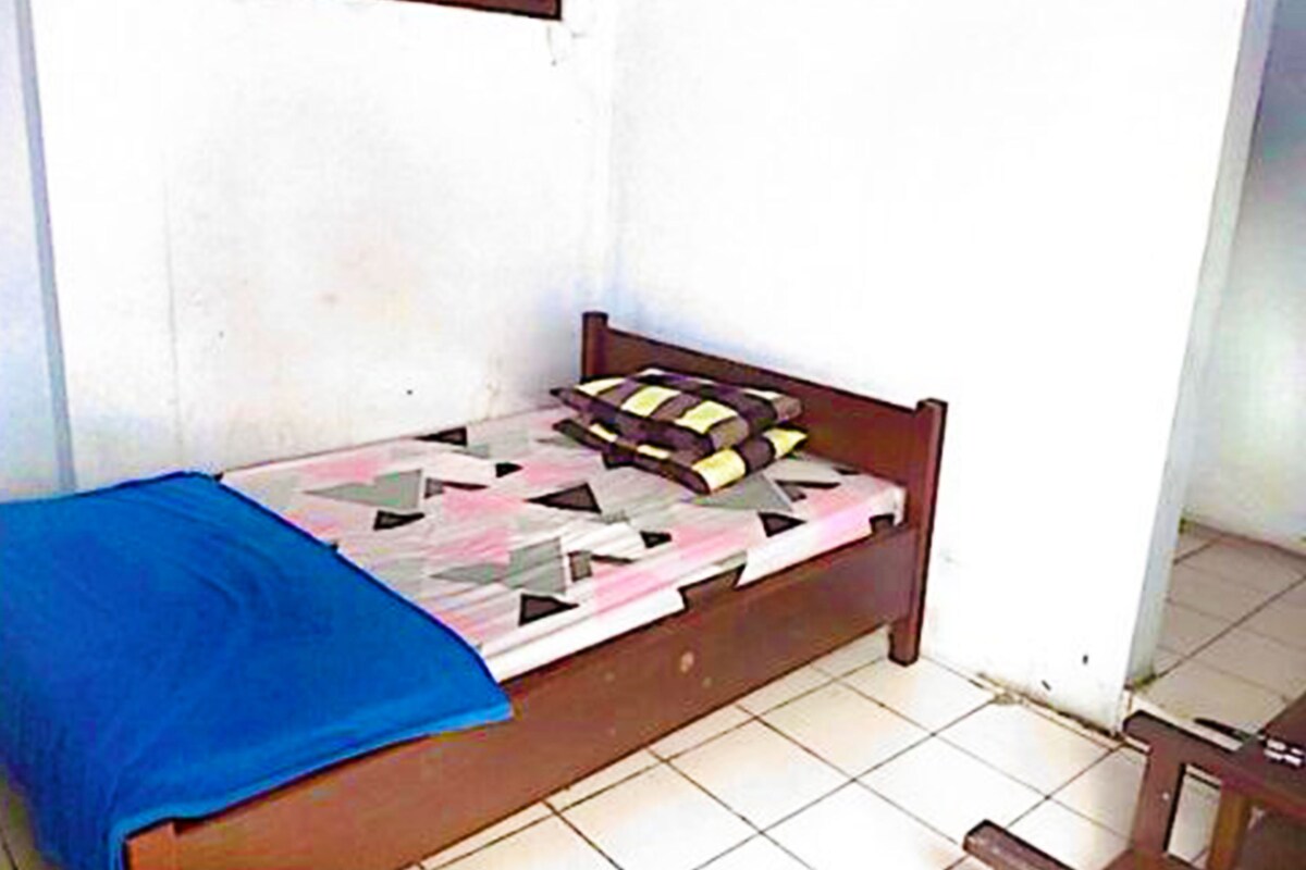 A small, single-bed room with a wooden headboard, a patterned bedspread, and a blue blanket.