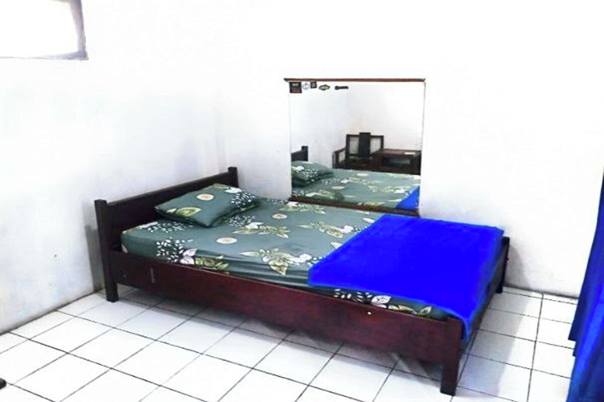 A single bed with a floral bedspread and a blue blanket, a wooden headboard, and a white tiled floor.