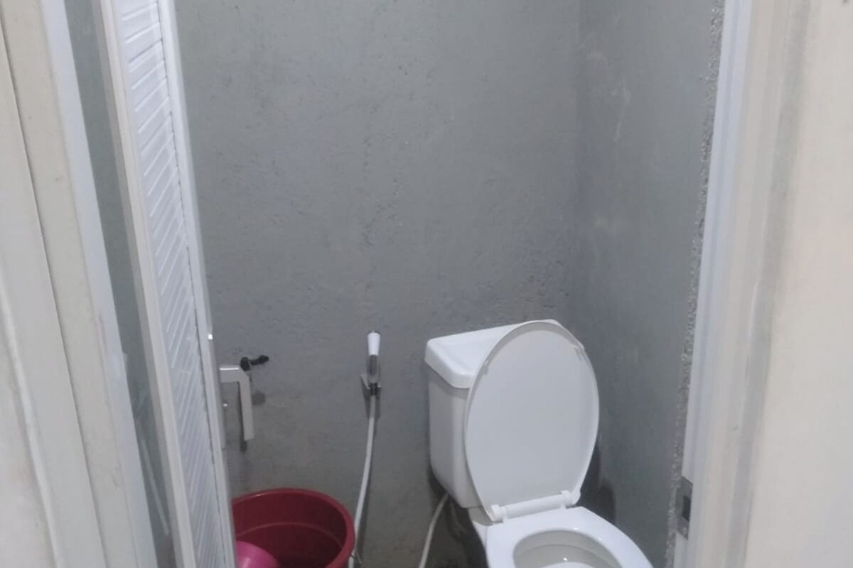 A small bathroom with a toilet, a red bucket, and a shower hose.