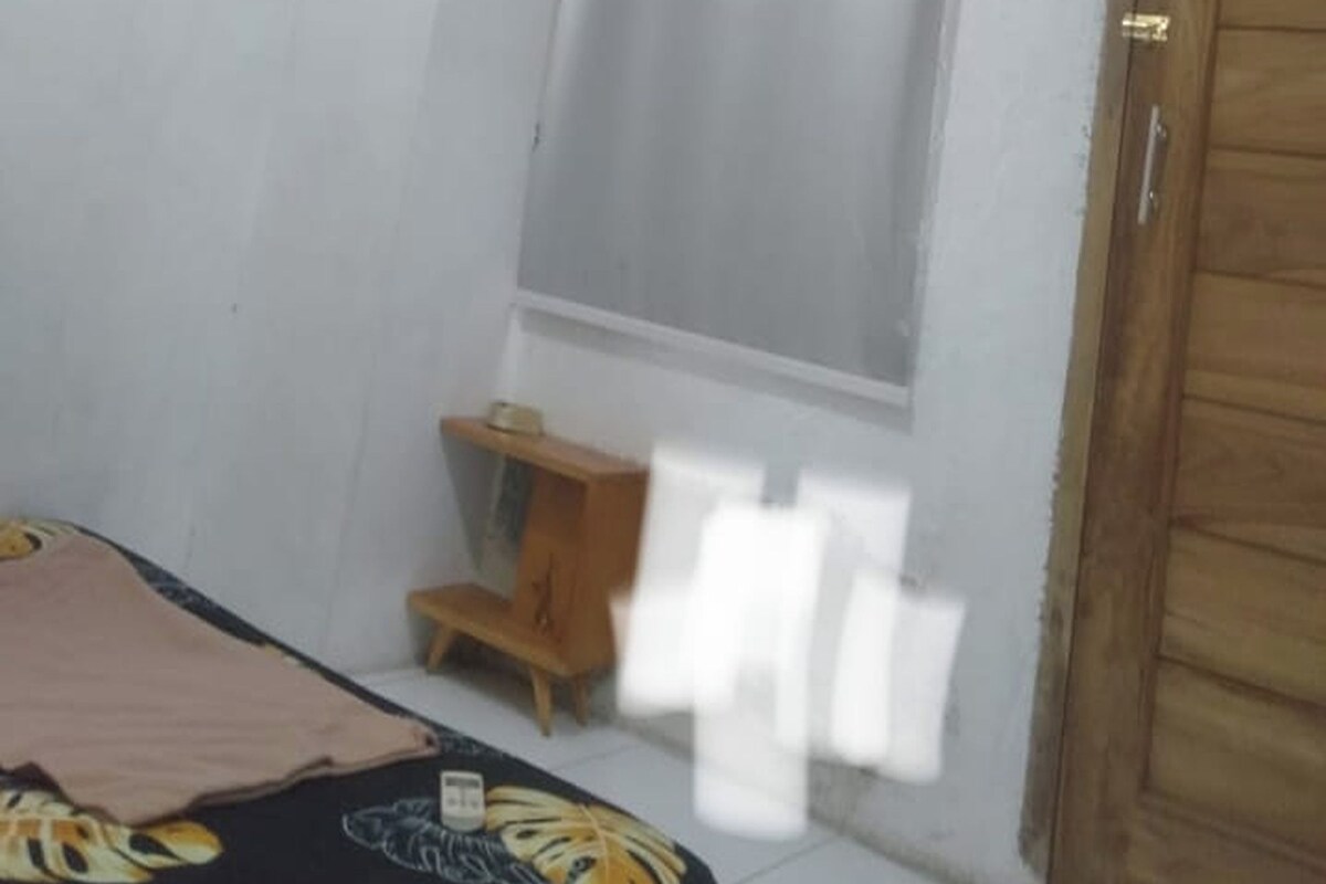 A room with a bed, a wooden cabinet, a window with a blind, and a door.