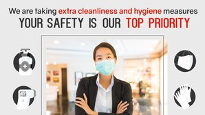 Une personne en costume, les bras croisés, se tient dans un espace intérieur bien éclairé, peut-être dans le hall d’un hôtel. Des icônes indiquent la présence de mesures d’hygiène, comme du gel hydroalcoolique, un masque et des gants.