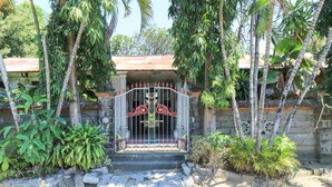 A gated entrance with a metal gate, surrounded by tropical vegetation and a stone wall. - Sari Bali Resort (Kuta)