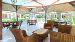 A covered outdoor seating area with wicker furniture and a glass table. - Sari Bali Resort (Kuta)