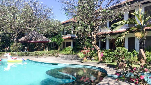 A swimming pool with a curved design, surrounded by lush greenery and a thatched-roof structure. - Sari Bali Resort (Kuta)