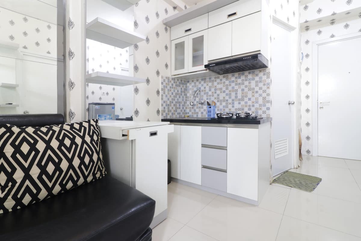 Een kleine keuken met witte kastjes, een zwart aanrecht en een decoratieve spatwand.