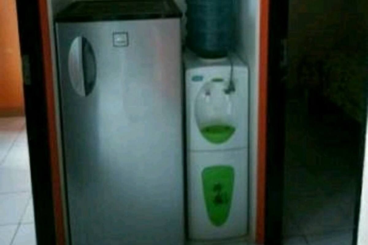A compact kitchen area with a refrigerator, a water dispenser, and a small cabinet.