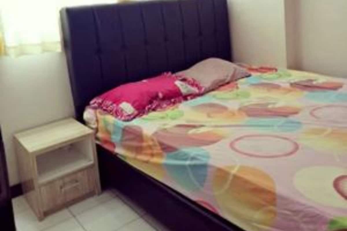 A bedroom with a bed, a nightstand, a window with curtains, and a wall-mounted air conditioner.