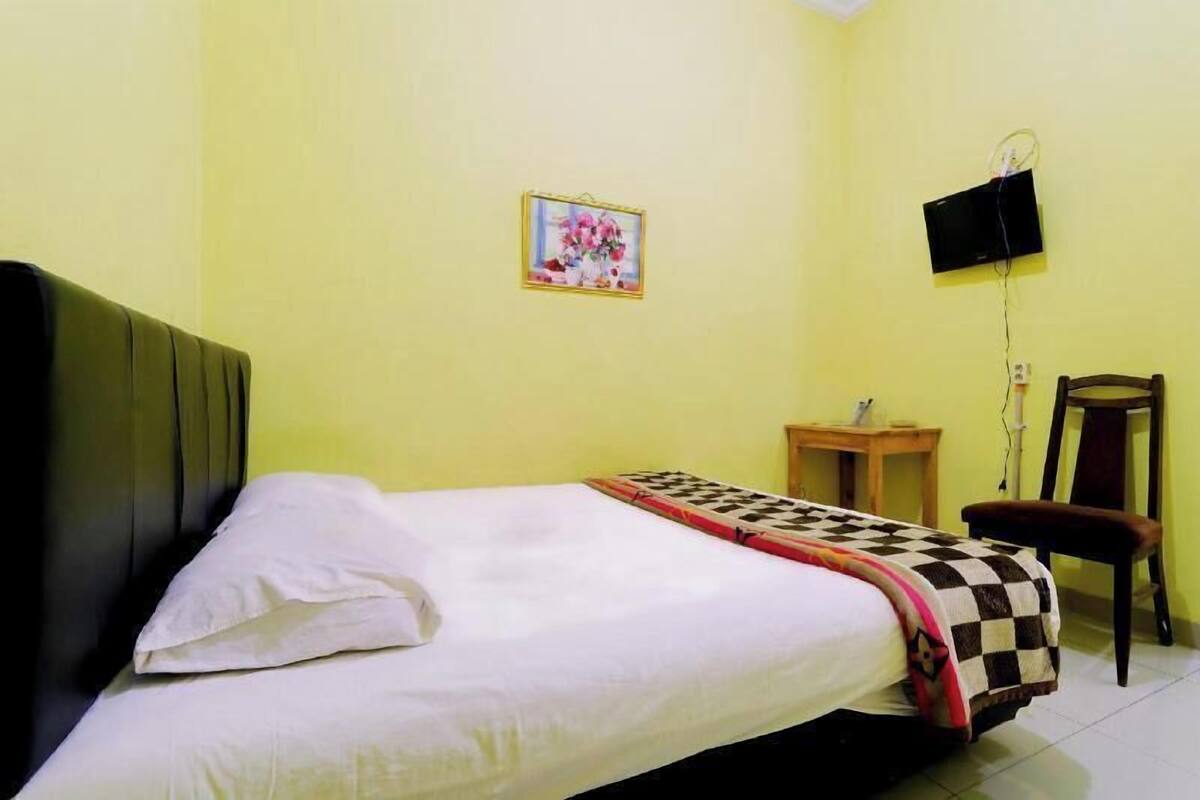 A room with a bed, a small table, a chair, a television mounted on the wall, and a framed picture on the wall.