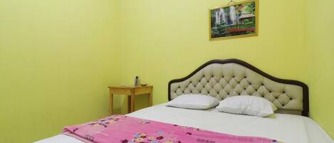 Una habitación con una cama, una mesita de noche de madera, un aire acondicionado de pared y un cuadro enmarcado.