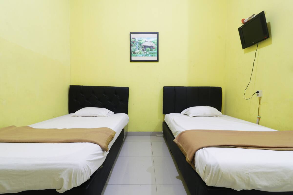 A room with two beds, a television mounted on the wall, and a framed picture above the beds.