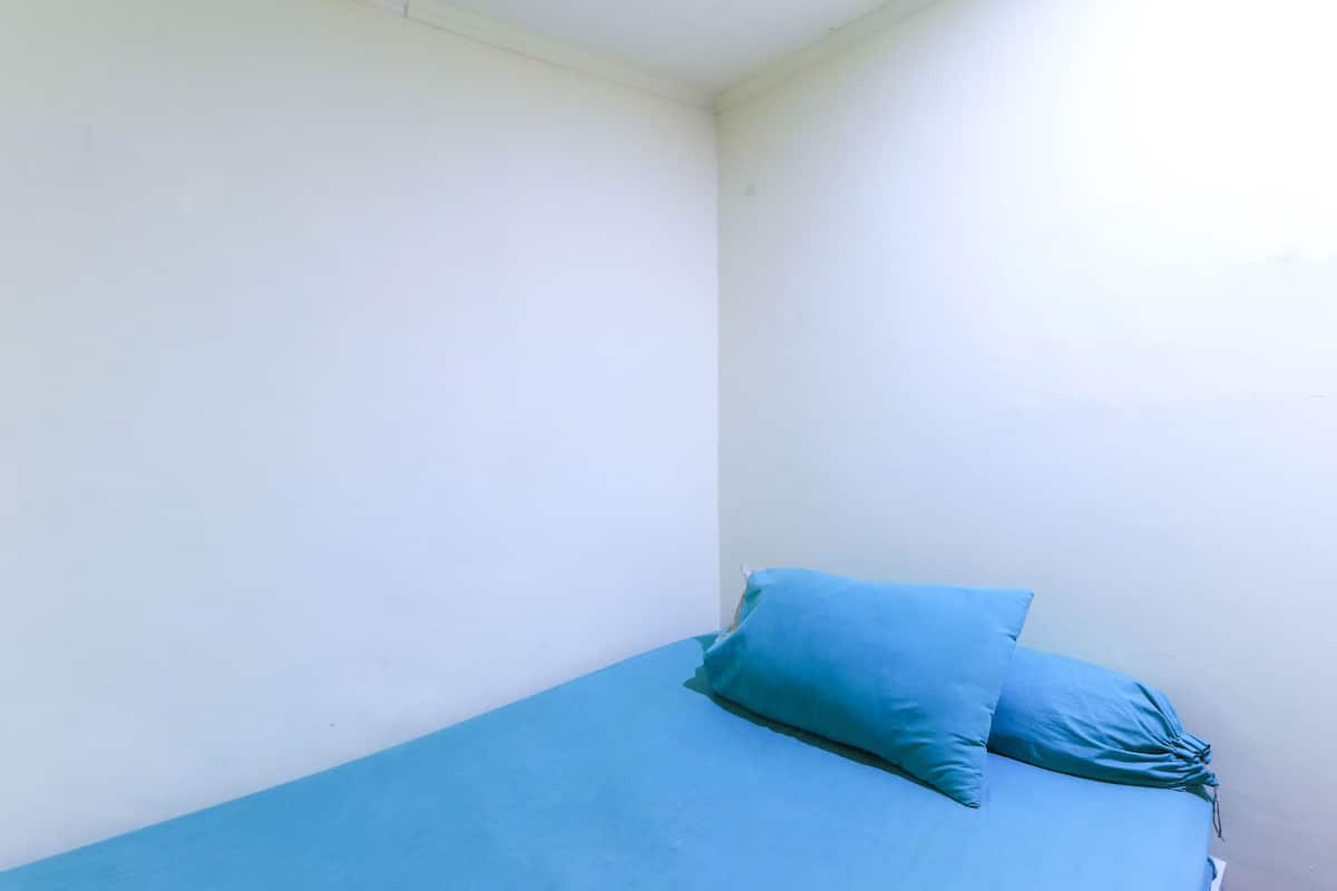 Una habitación pequeña con una cama individual, colchón y almohadas azules.