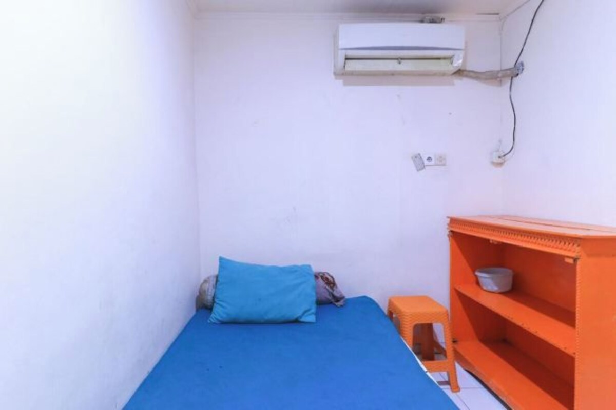 A small room with a single bed, an air conditioning unit, a stool, and a shelf unit.