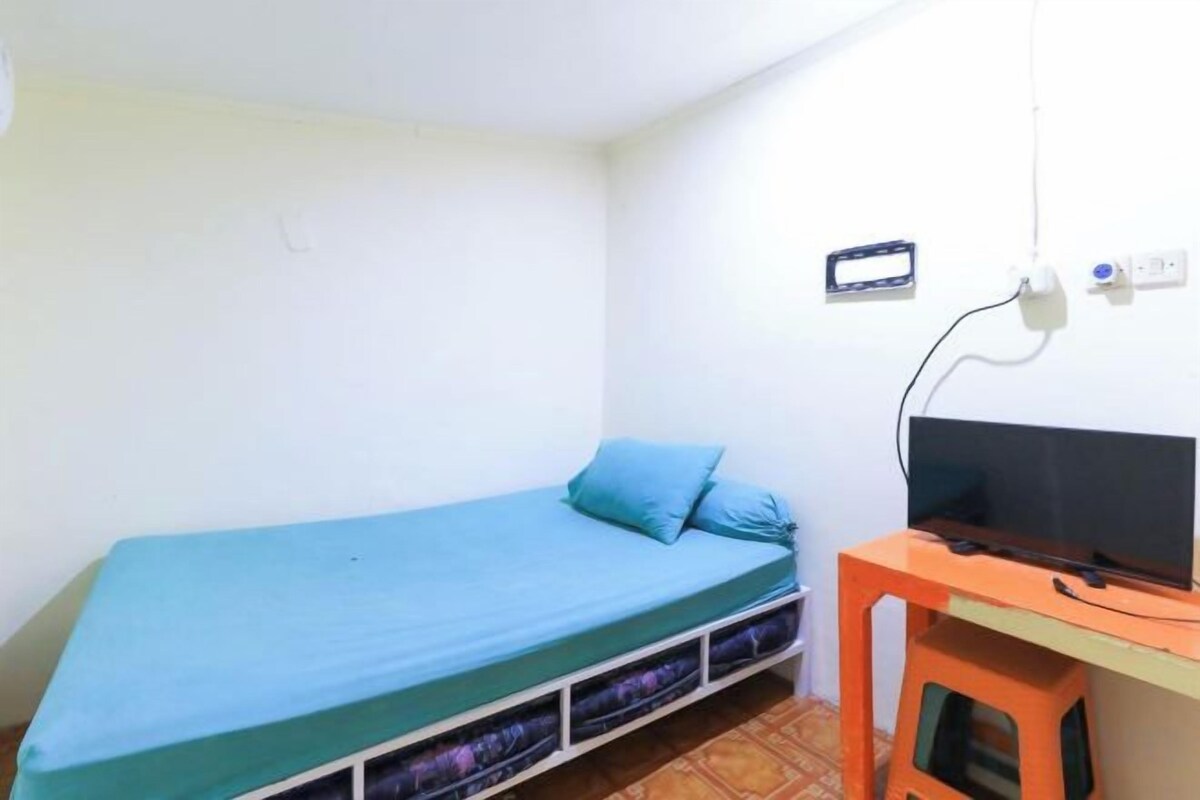 Una stanza piccola con un letto singolo, una scrivania con un computer e una televisione.