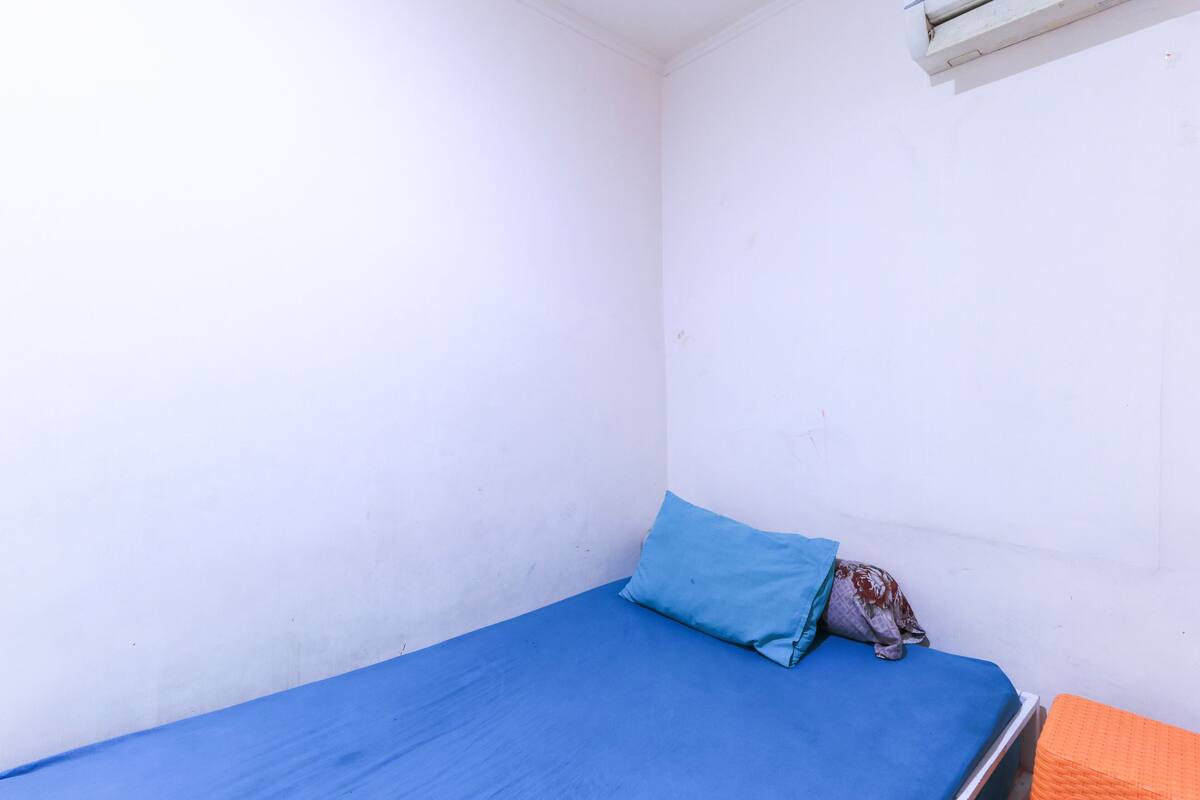 Una habitación pequeña con una cama individual, colchón azul y una almohada.