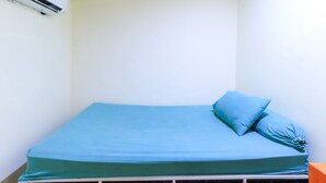 A small, single-bed room with a blue mattress and matching pillow, white walls, and a white ceiling. - Techno Inn (Makassar)