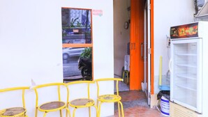A small shop with a yellow chair outside, a refrigerator inside, and a door with a sign. - Techno Inn (Makassar)