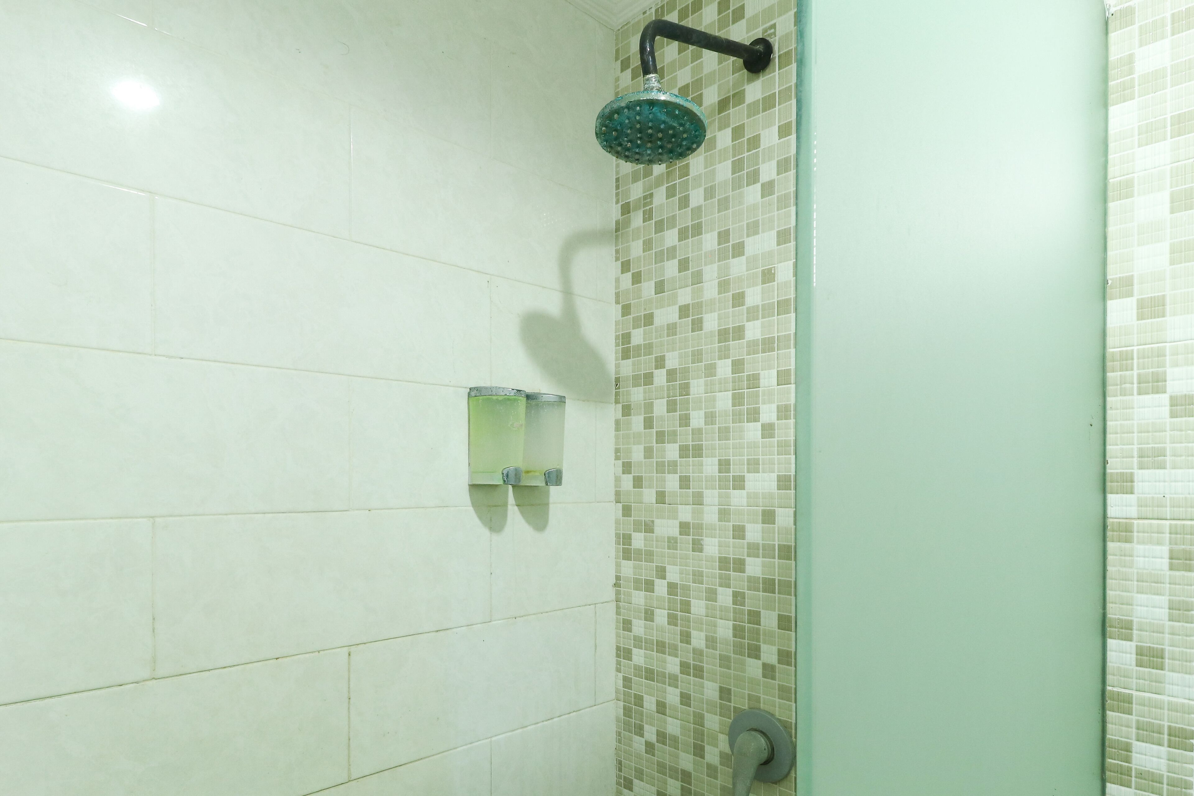 A bathroom with white tiles, a shower with a green showerhead, and a glass-enclosed sink.