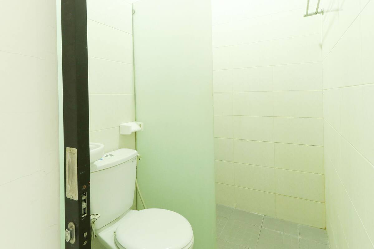 A small, enclosed bathroom with a toilet, a white sink, and a shower area.