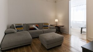 Un salon moderne avec un canapé gris, un pouf assorti et une petite table d’appoint sur laquelle se trouve une lampe.