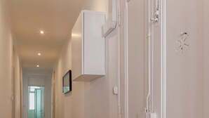 Un couloir doté d’un plancher en bois, de murs blancs et d’une porte blanche sur laquelle est fixée une petite boîte électrique.