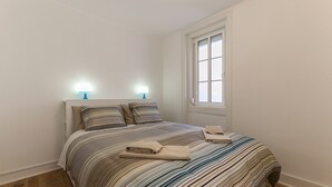 Une chambre à coucher avec un lit, deux lampes de chevet, une fenêtre et un plancher en bois.