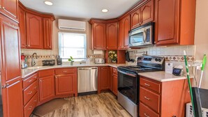 A kitchen with wooden cabinets, a stainless steel dishwasher, a microwave, and a stove. - Great Family Times In this lovely Cape with Resort style backyard (Massapequa)