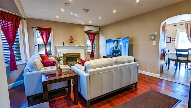 A living room with a sofa, a fireplace, a television, and a dining area. - Great Family Times In this lovely Cape with Resort style backyard (Massapequa)