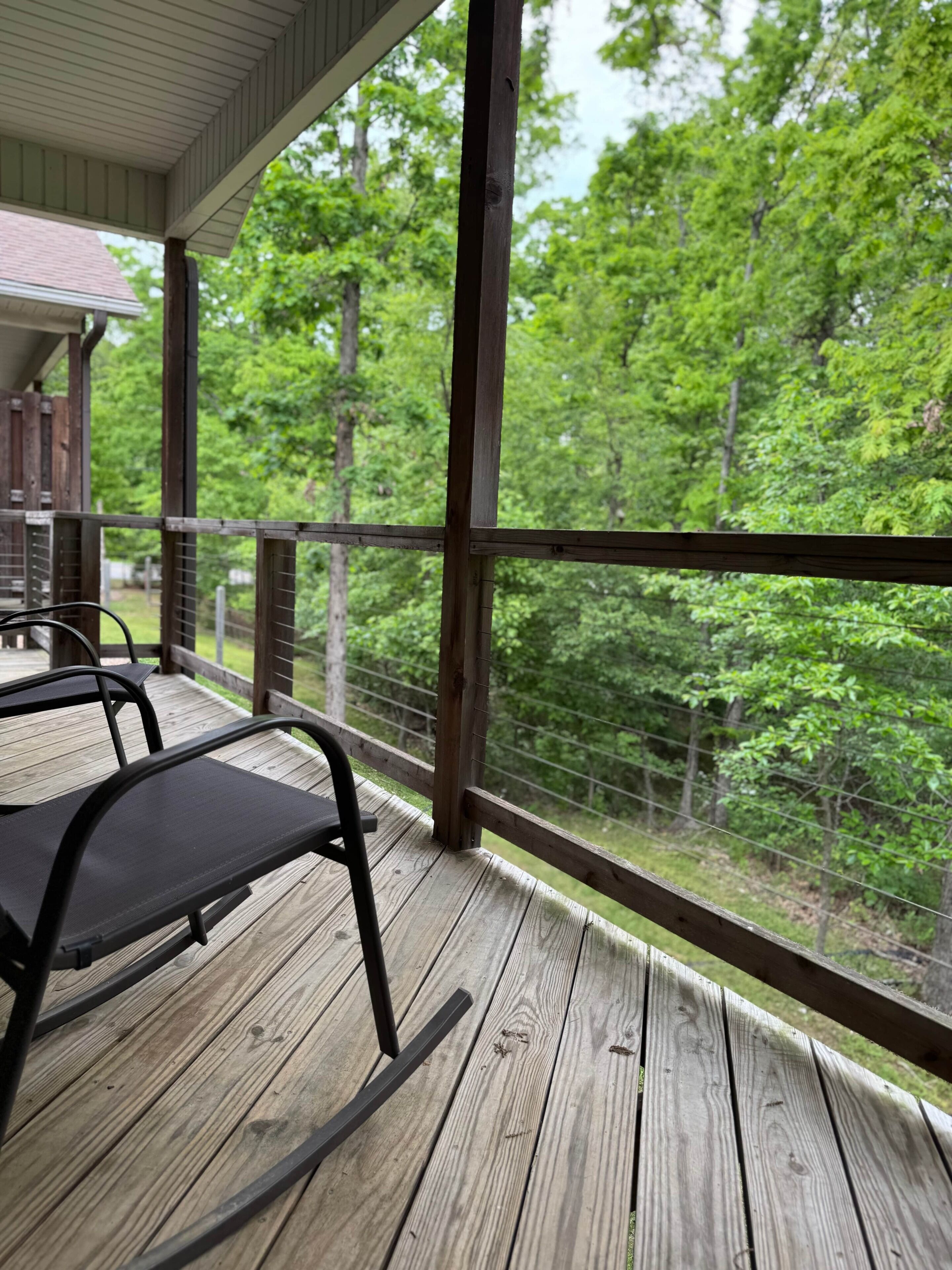 A wooden deck with metal chairs, overlooking a forested area.