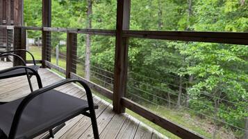 A wooden deck with metal chairs, overlooking a forested area.