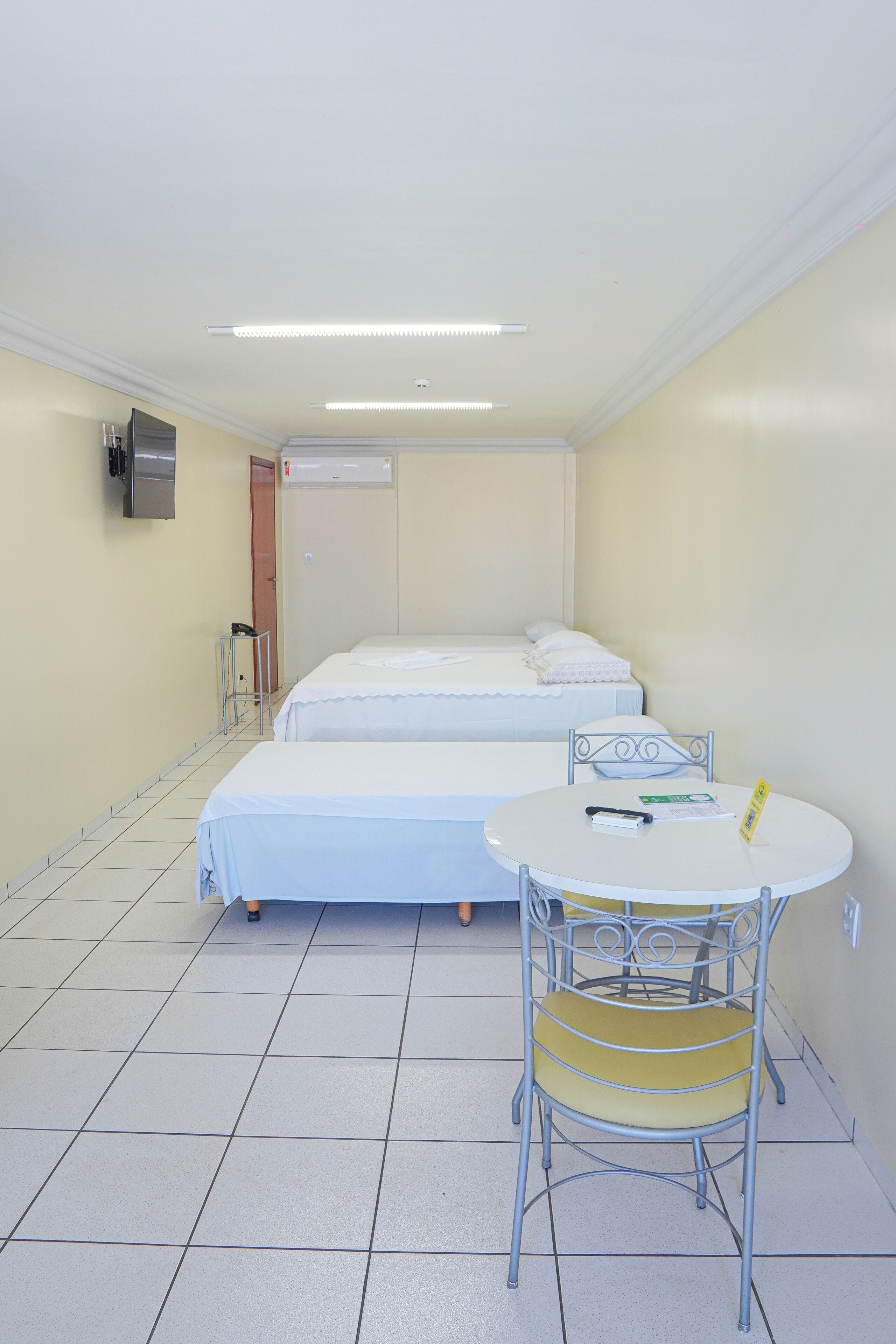 A small, clean room with two beds, a round table with a chair, and a television on the wall.