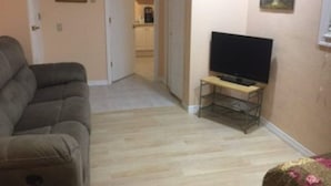 A living room with a sofa, a television on a stand, a door leading to a kitchen, and a painting on the wall. - Perfect getaway! Newly remodeled waterfront suite. (North Port)