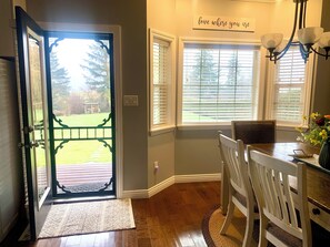 An open door leading to a patio with a view of a lawn and trees, a dining area with a table and chairs, and a wall-mounted sign that reads "love where you are". - Spacious  3 bedroom Guest home with large swim spa and a fire-pit! (Hope)