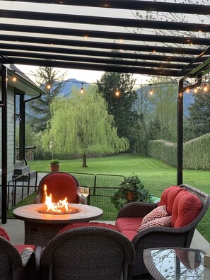 Relax by the fire pit in a serene outdoor seating area surrounded by a pergola and lush greenery.