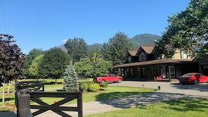Un bâtiment à deux étages avec un porche, une voiture rouge garée devant, et une montagne en arrière-plan.