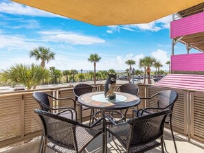 An outdoor patio with a round table and chairs, palm trees, and a view of the beach.