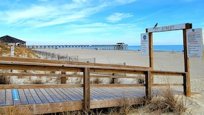 Una pasarela de madera que conduce a una playa, con un muelle al fondo.