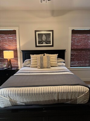 A neatly made bed with a striped bedspread and multiple pillows, a framed picture above the bed, and a lamp on a bedside table.