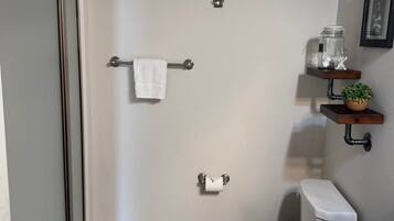 Un baño con inodoro, un perchero, una estantería con una planta y un cuadro en la pared.