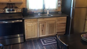 Une cuisine avec des meubles de rangement en bois, un réfrigérateur en acier inoxydable, une cuisinière et une fenêtre avec des rideaux.