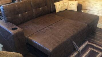 Un sofá de cuero marrón con una mesita de centro integrada, un sillón estampado y una alfombra tejida sobre un piso de madera.