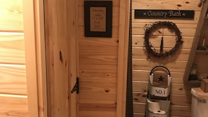 Un intérieur en bois avec une porte, une pancarte sur laquelle on peut lire « Chaque jour est un cadeau de Dieu », une autre pancarte indiquant « Bain à la campagne », et une couronne décorative accrochée au mur.