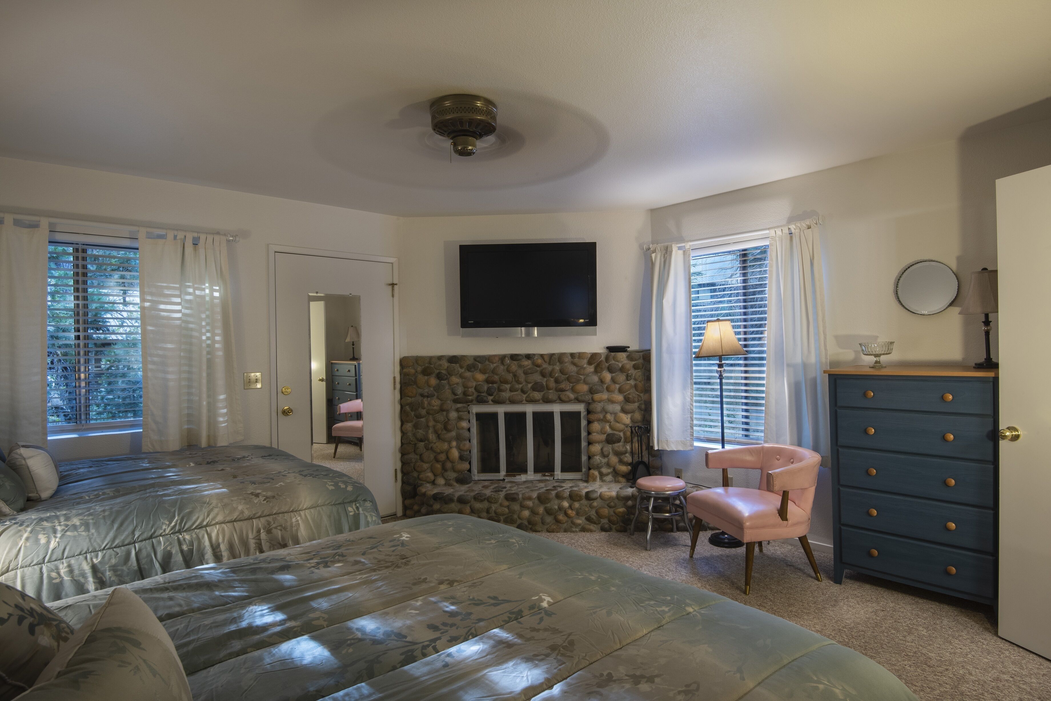 A bedroom with two beds, a stone fireplace, a television, a dresser, and a chair.