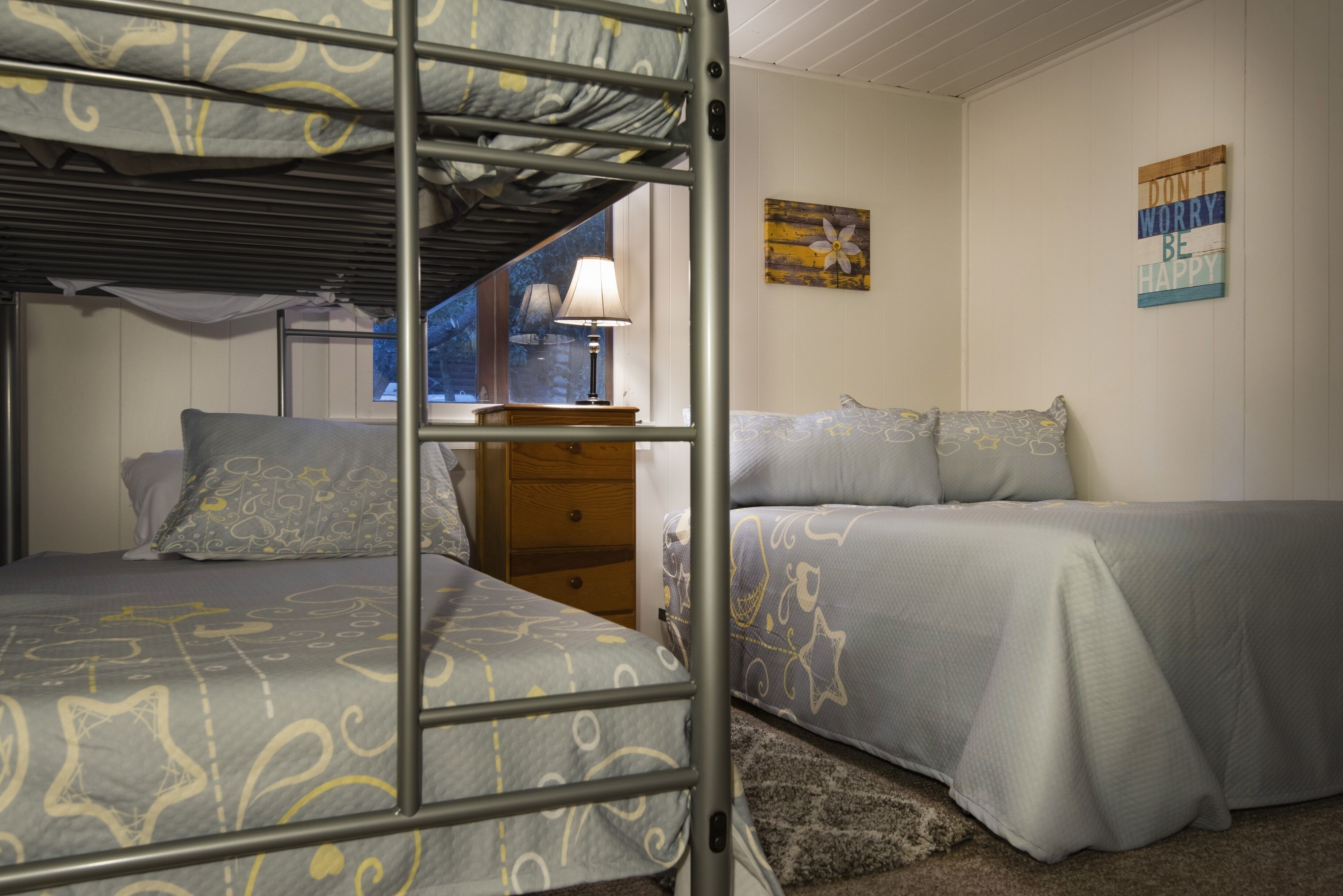 Une chambre avec un lit superposé, une fenêtre, une lampe, une commode en bois et une affiche motivante.